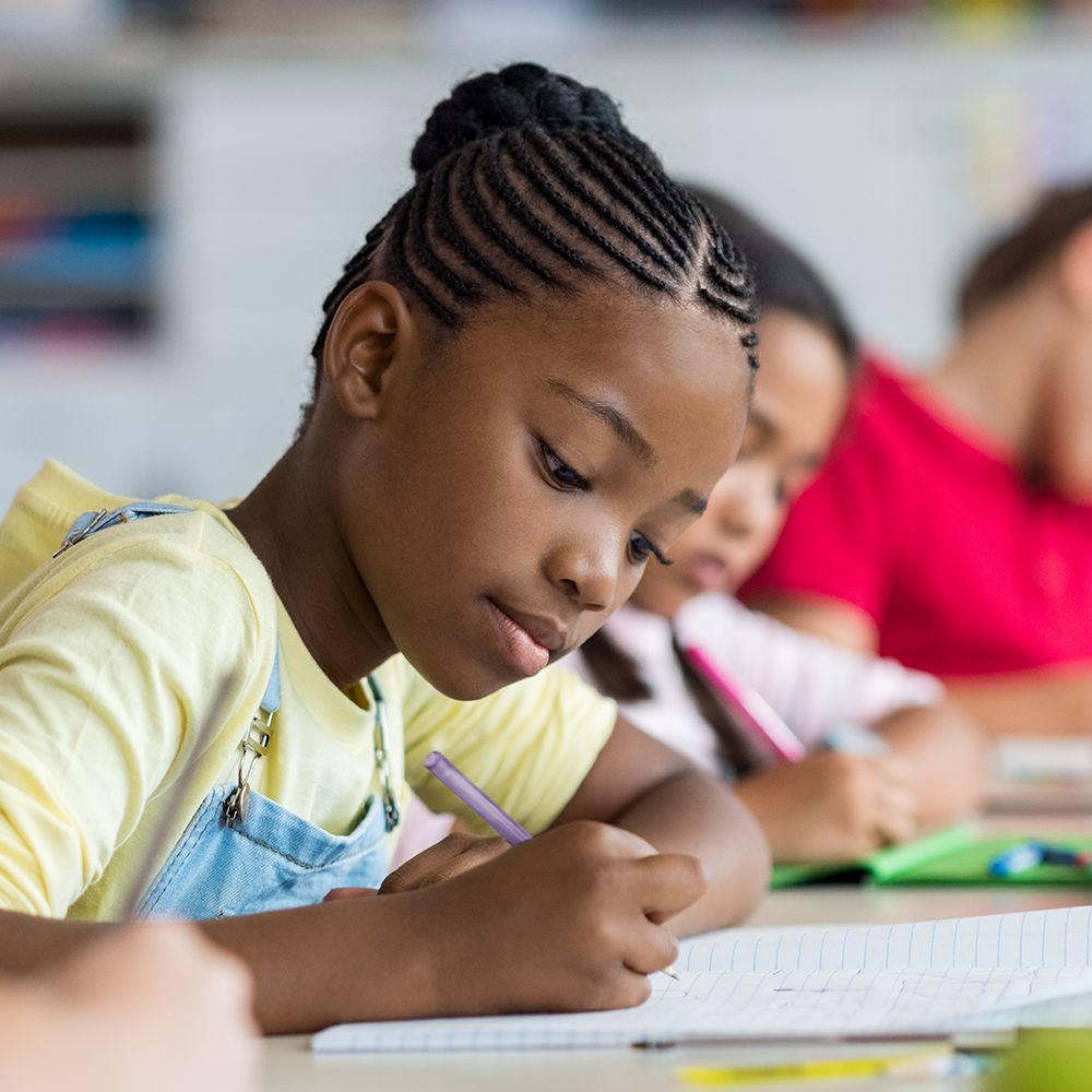 An image of a young African American girl at school, writing on a piece of paper.