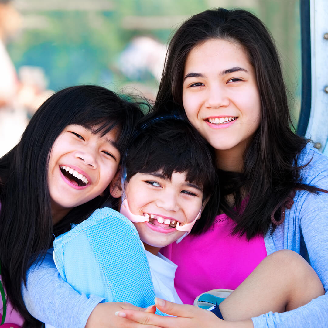 Three children smiling and hugging while looking at camera